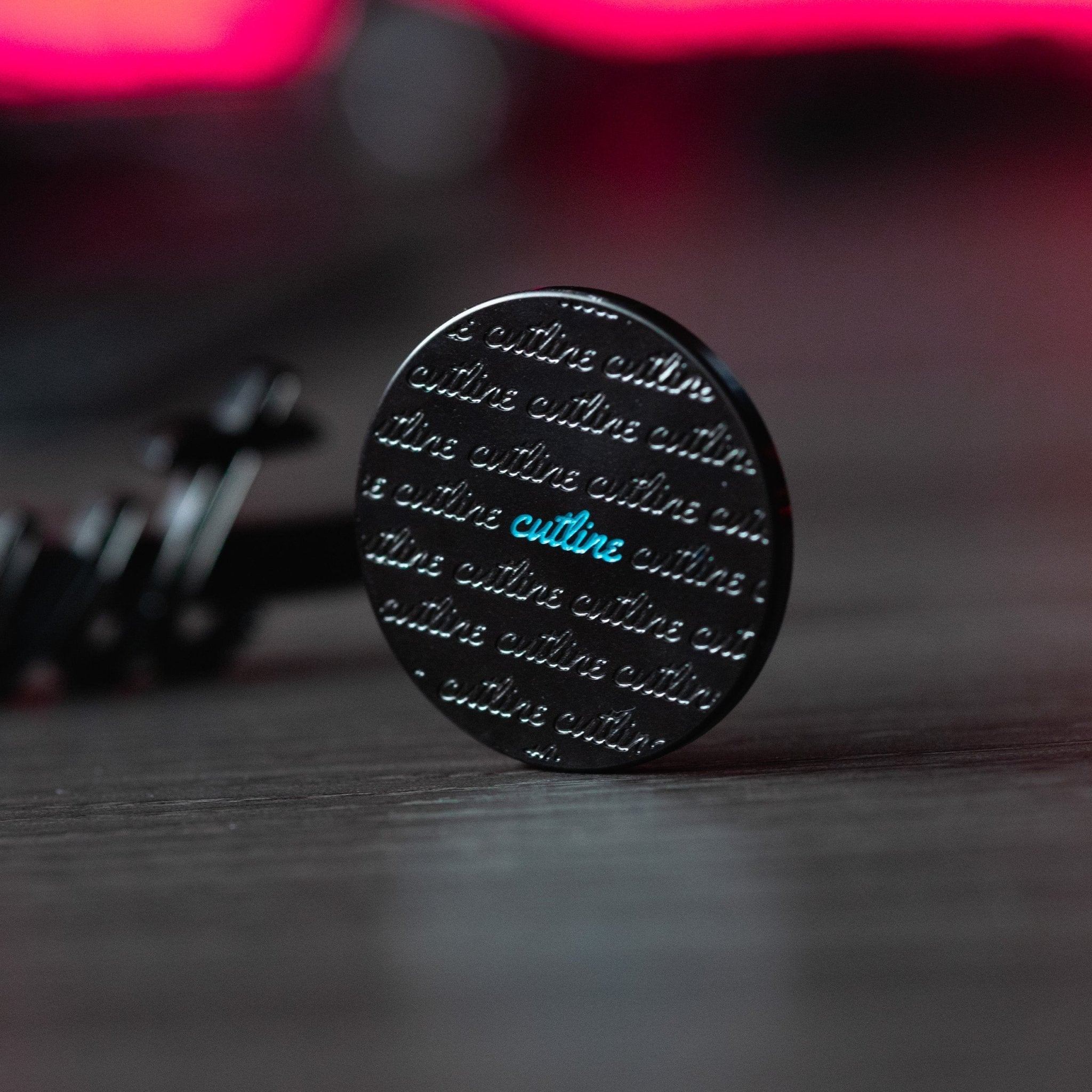 Cut "LINE" Alignment Ball Marker showing black design with repeated script and blue highlight on a wood surface background.