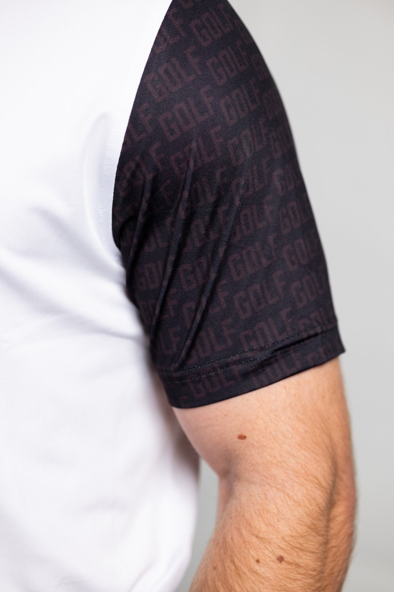 Close-up of black patterned sleeve detail on a white GOLF Arm Whiteout Polo worn by a person