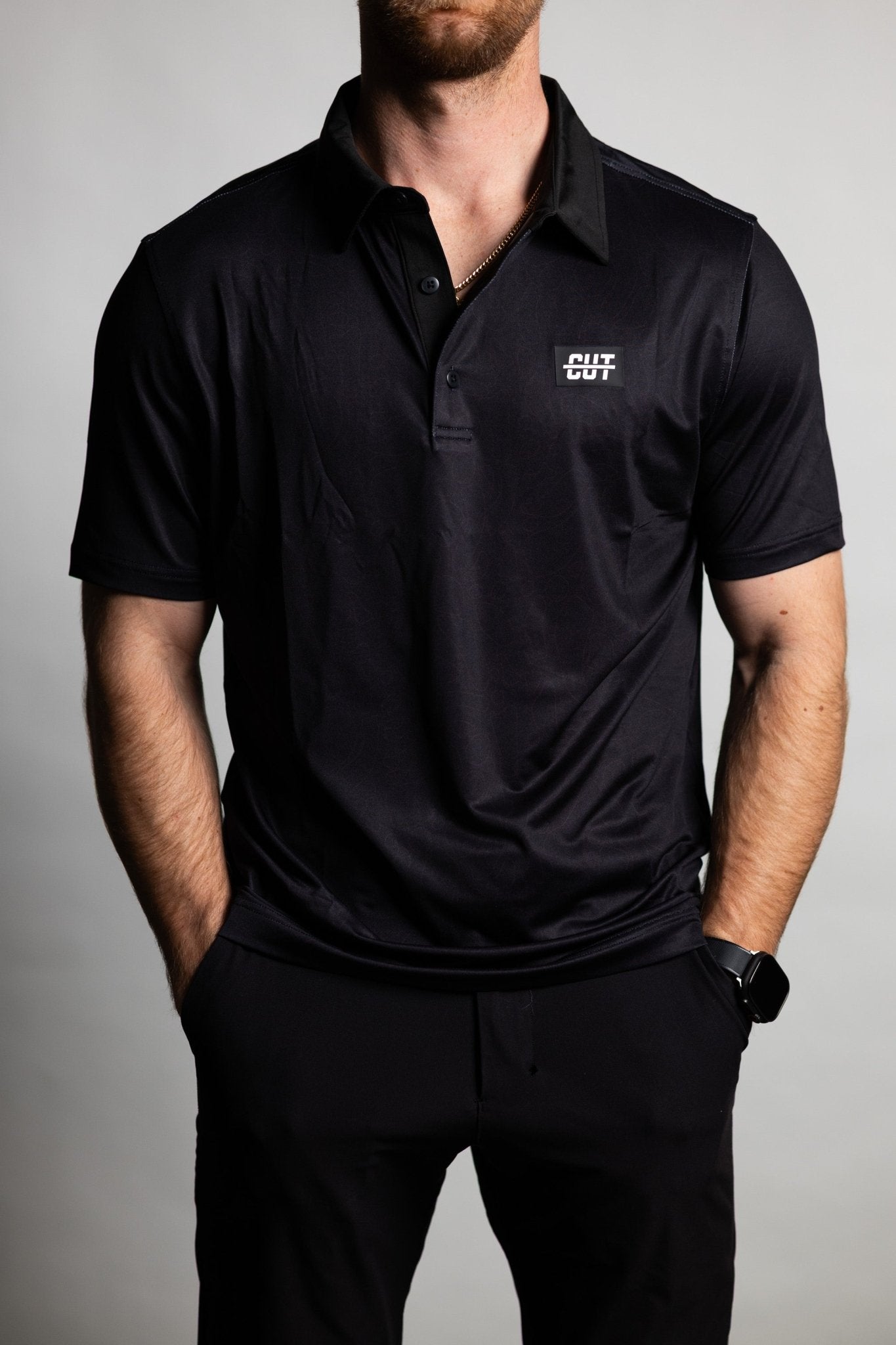 Man wearing a black Deep Topo Black Polo with short sleeves and a small logo on the chest posing with hands in pockets