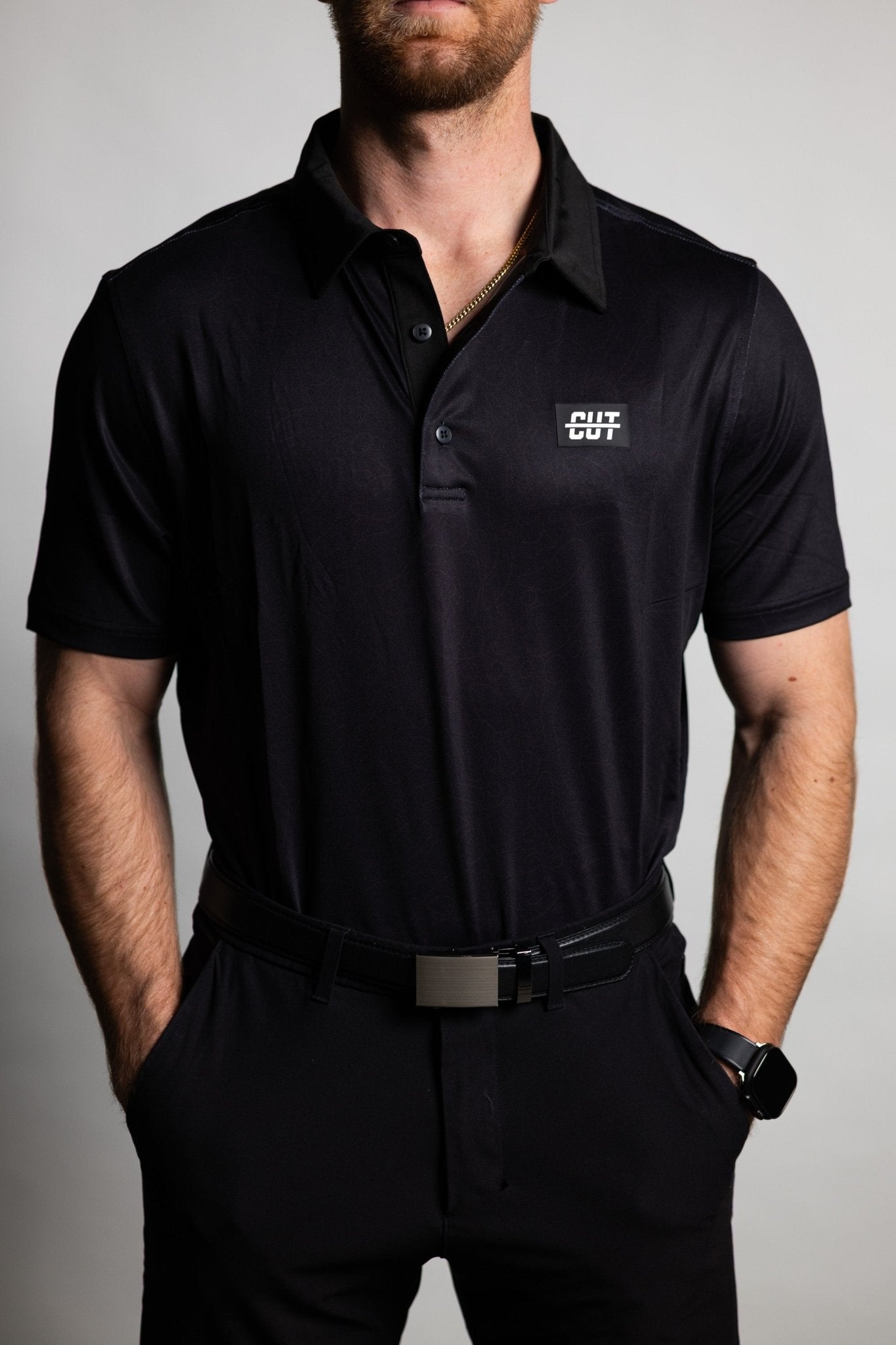 Man wearing a Deep Topo Black Polo with short sleeves and a small logo on the chest, styled for golf apparel.