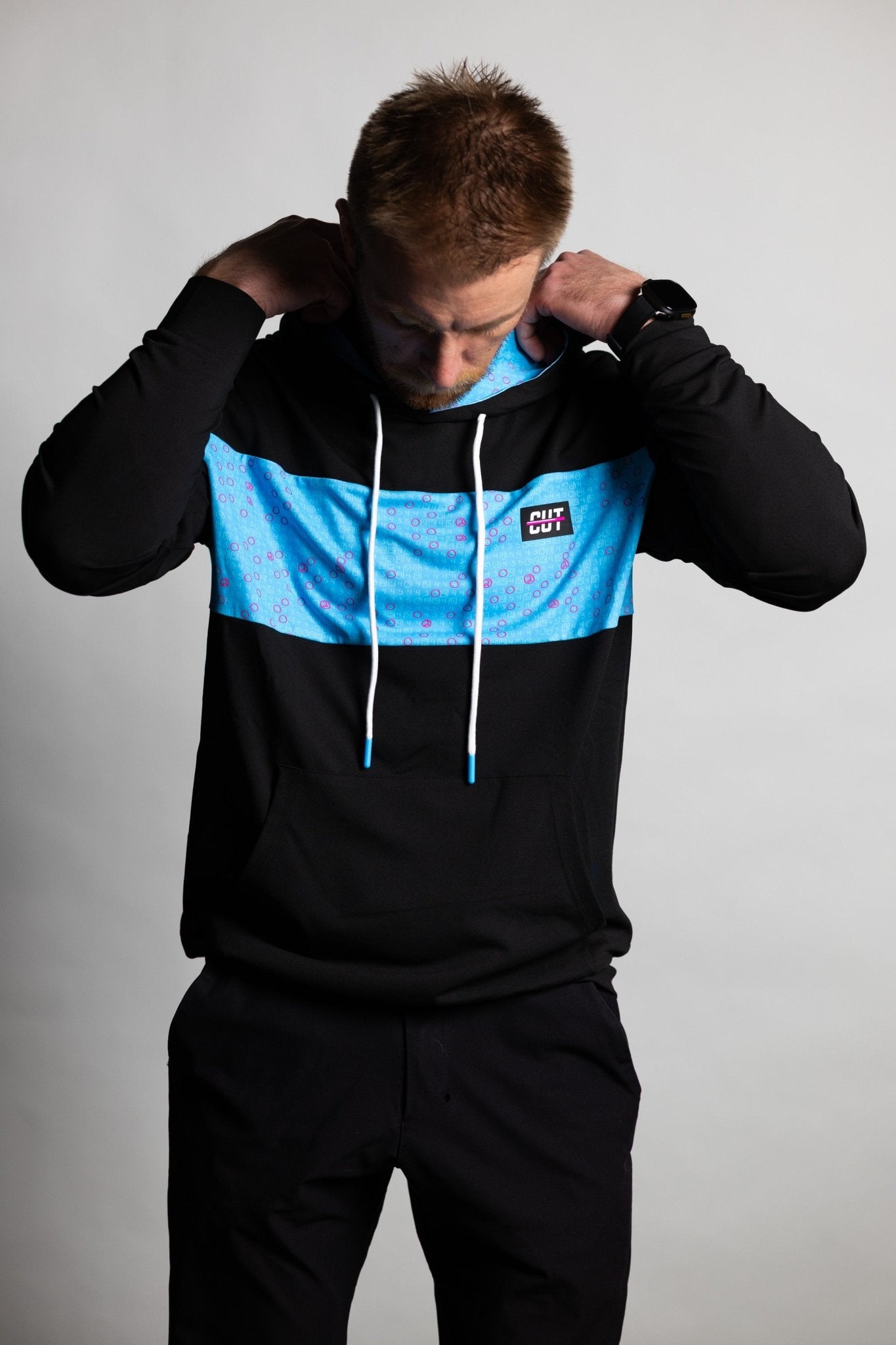 Man adjusting hood wearing Teal Scorecard Athletic Hoodie with black and teal color block and white drawstrings