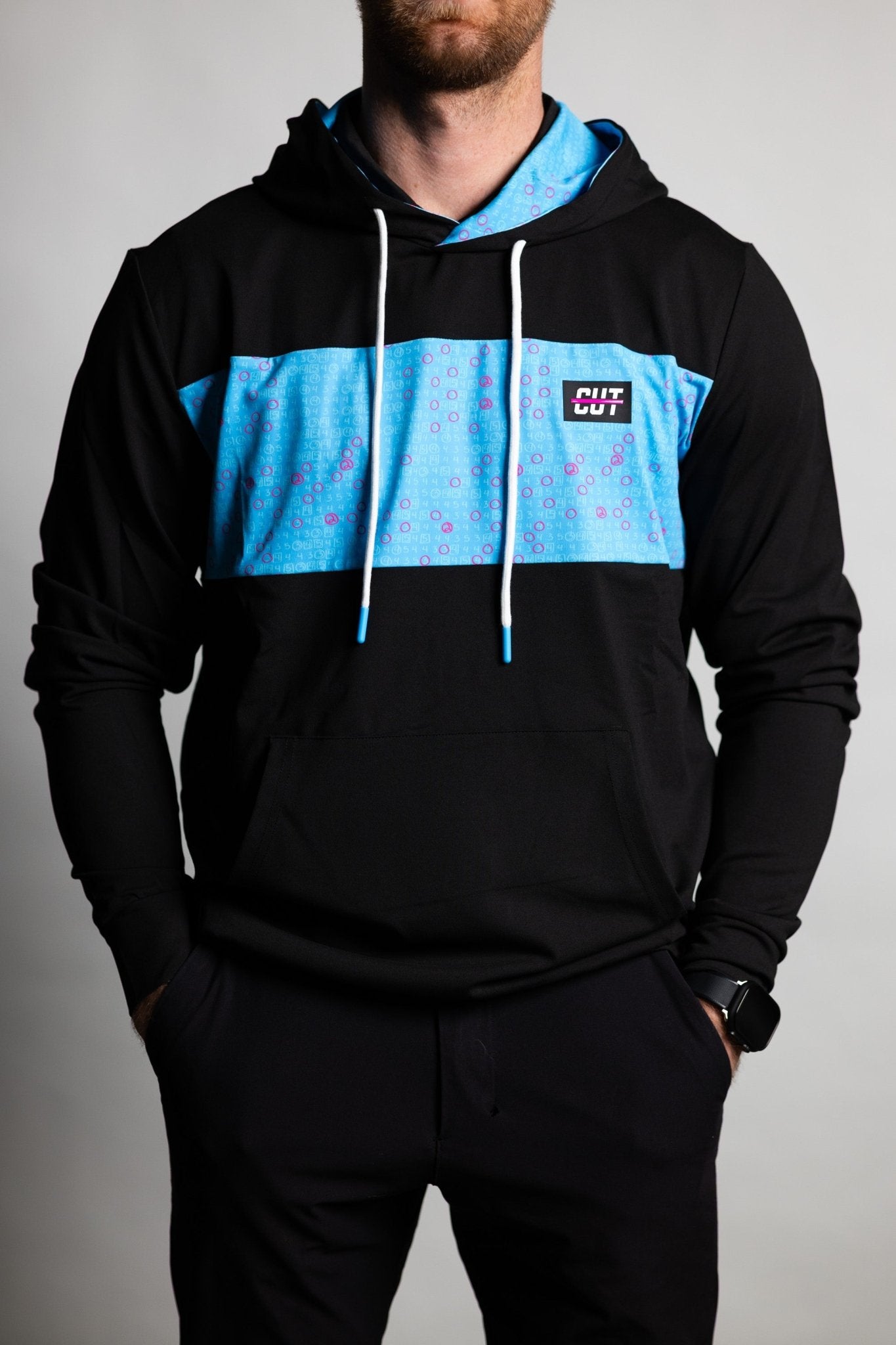 Man wearing black and blue Teal Scorecard Athletic Hoodie with hood and front pocket, posing with hands in pockets
