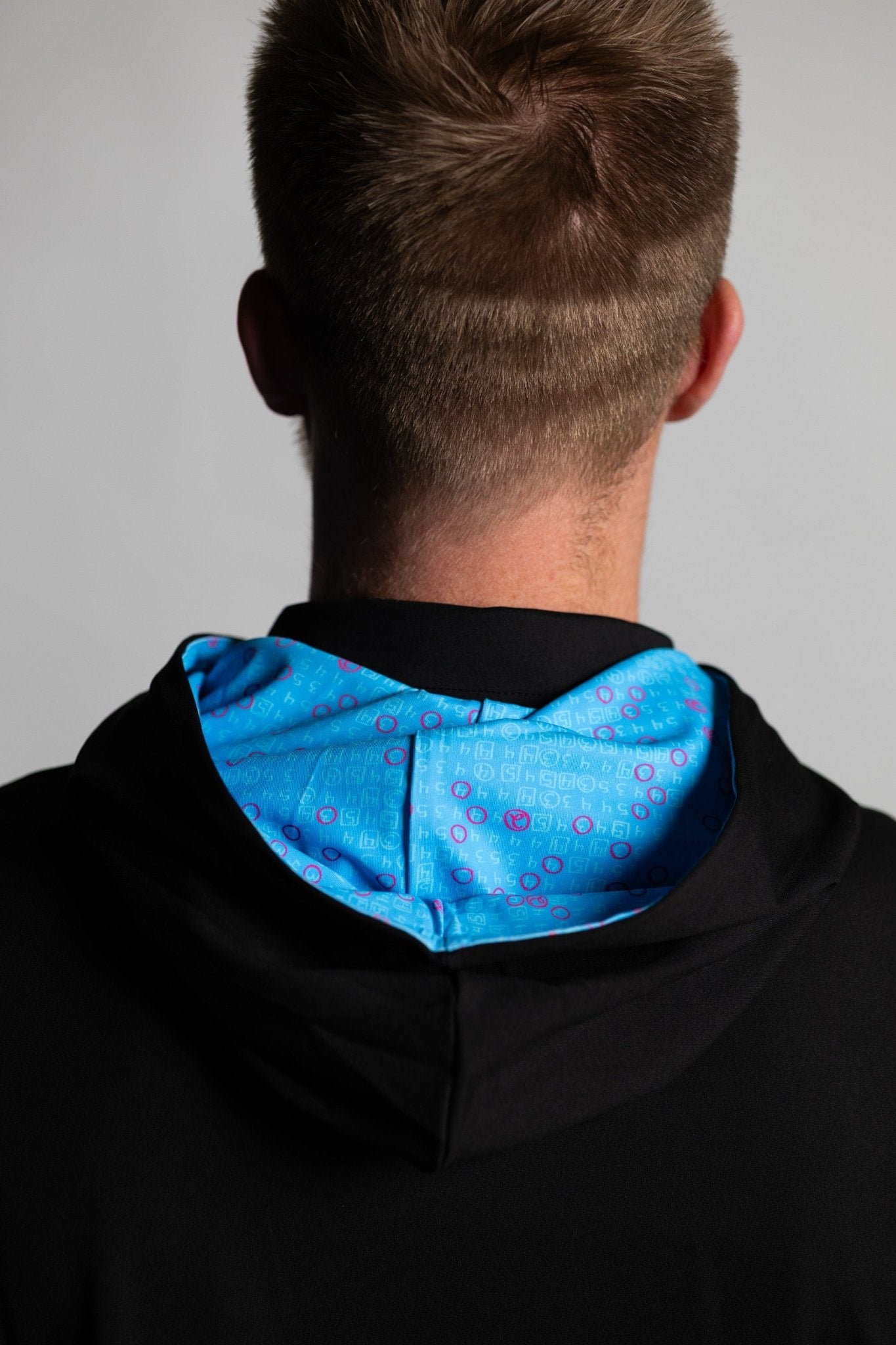 Back view of a man wearing Teal Scorecard Athletic Hoodie with a bright teal patterned hood lining in golf apparel style