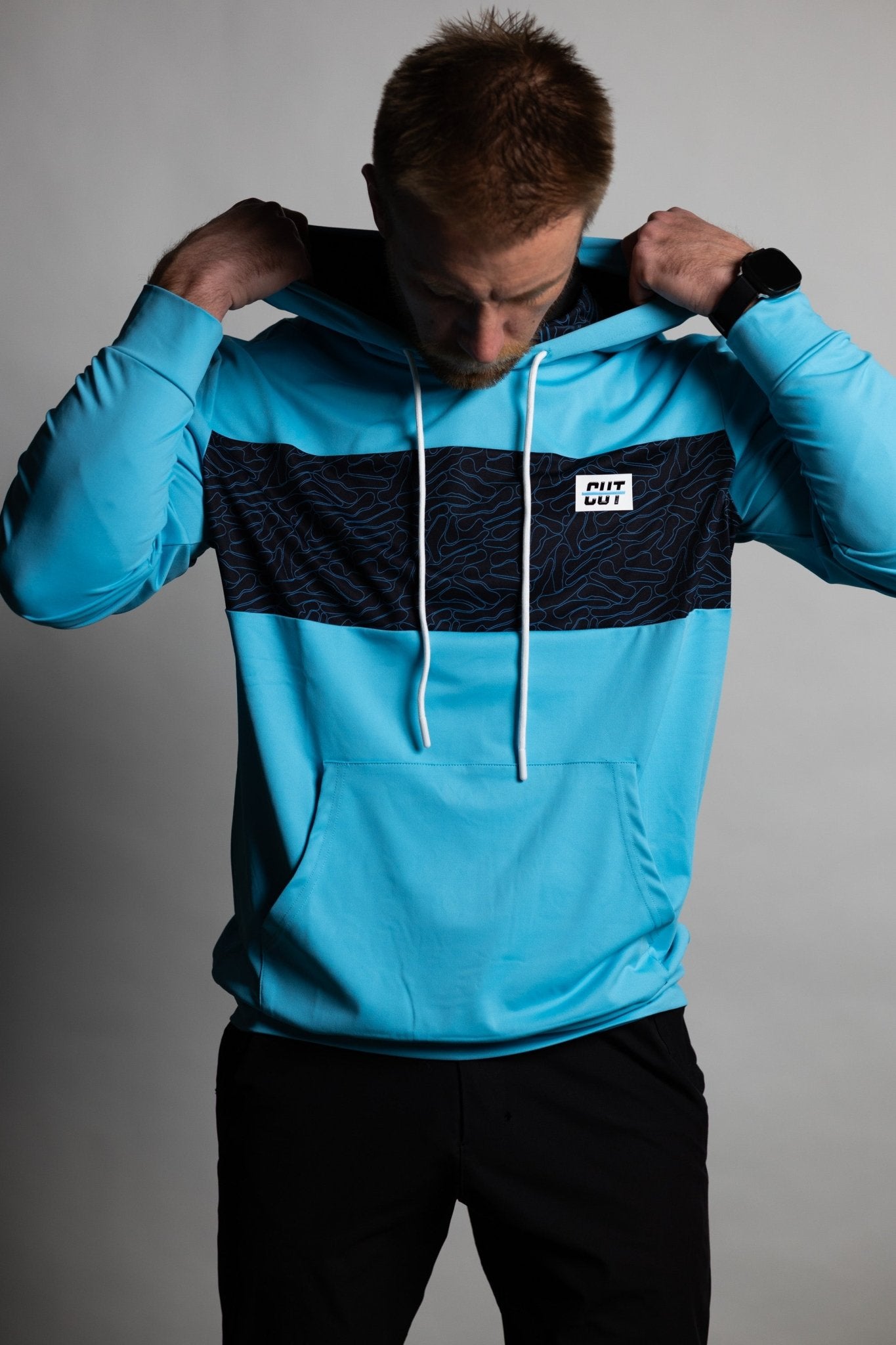 Man adjusting hood wearing a teal and black Teal Topo Athletic Hoodie with white drawstrings and front pocket