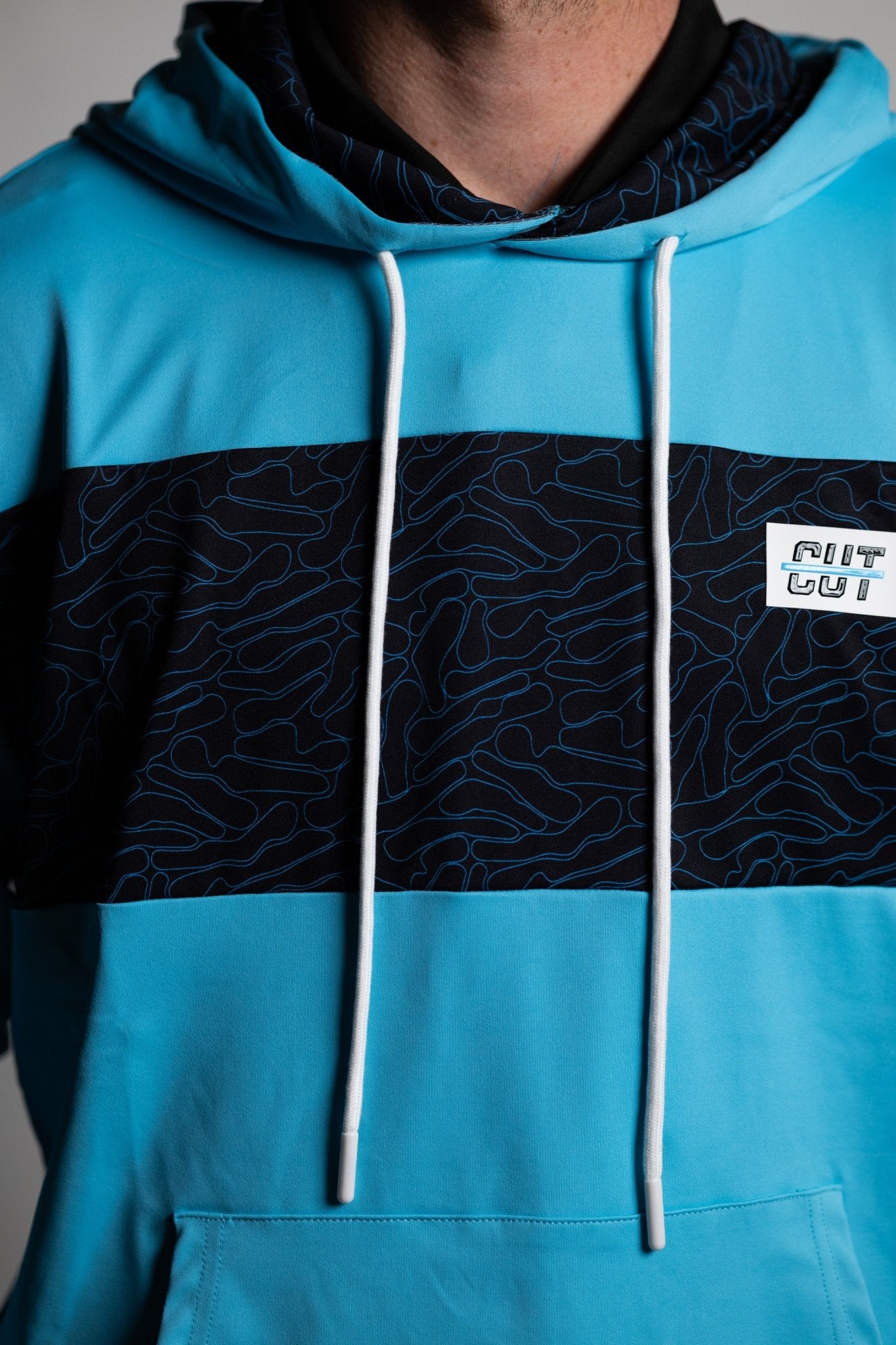 Close-up of a teal and black patterned Teal Topo Athletic Hoodie with white drawstrings and a logo patch on chest.