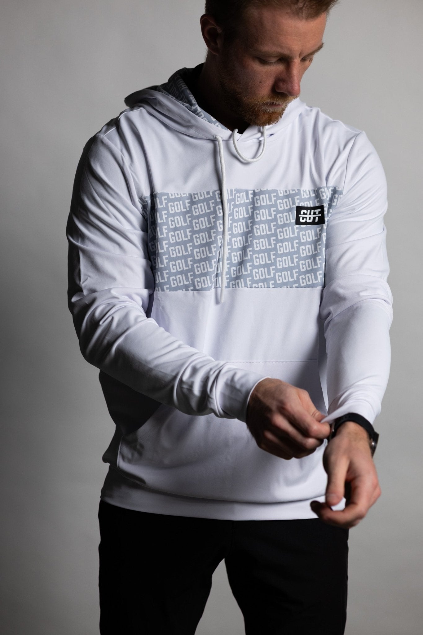 Man adjusting sleeve wearing GOLF Whiteout Athletic Hoodie with golf-themed design across chest and hood strings