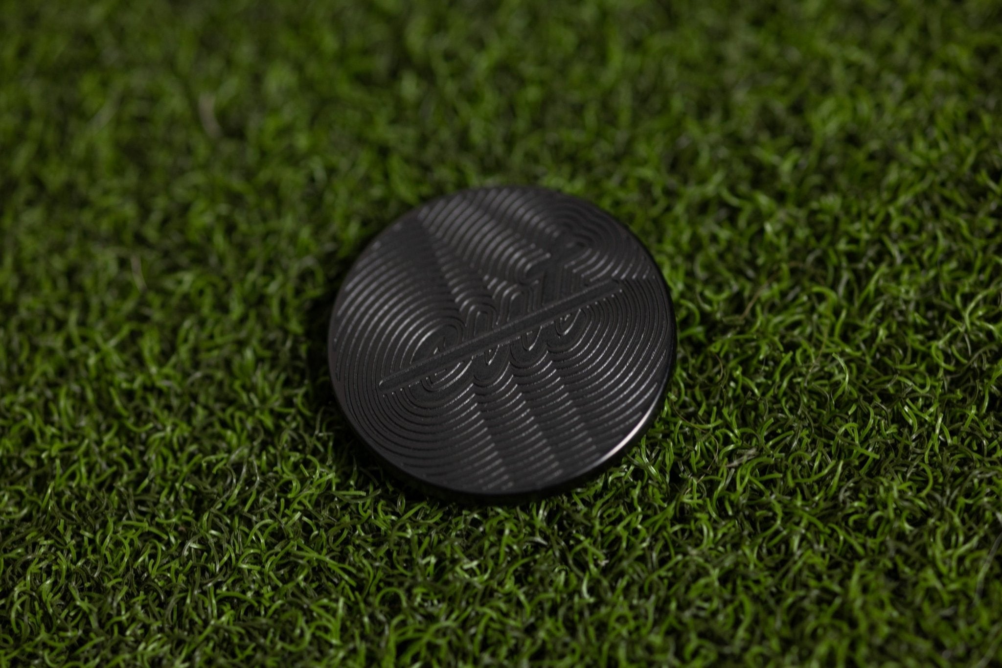 Cut "LINE" Alignment Ball Marker in black with textured circular design on green grass for golf gear accessory