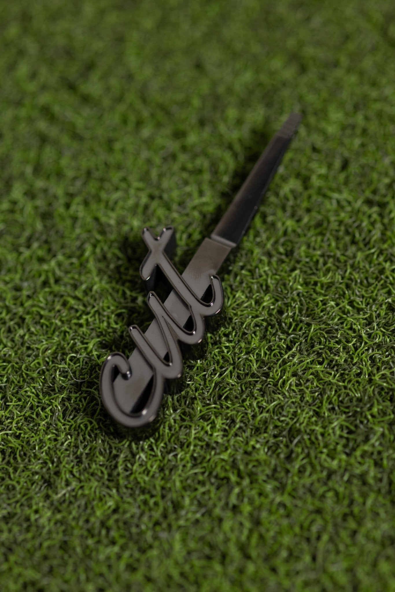 CUT Script Black Divot Tool with sleek black finish resting on green golf turf grass surface