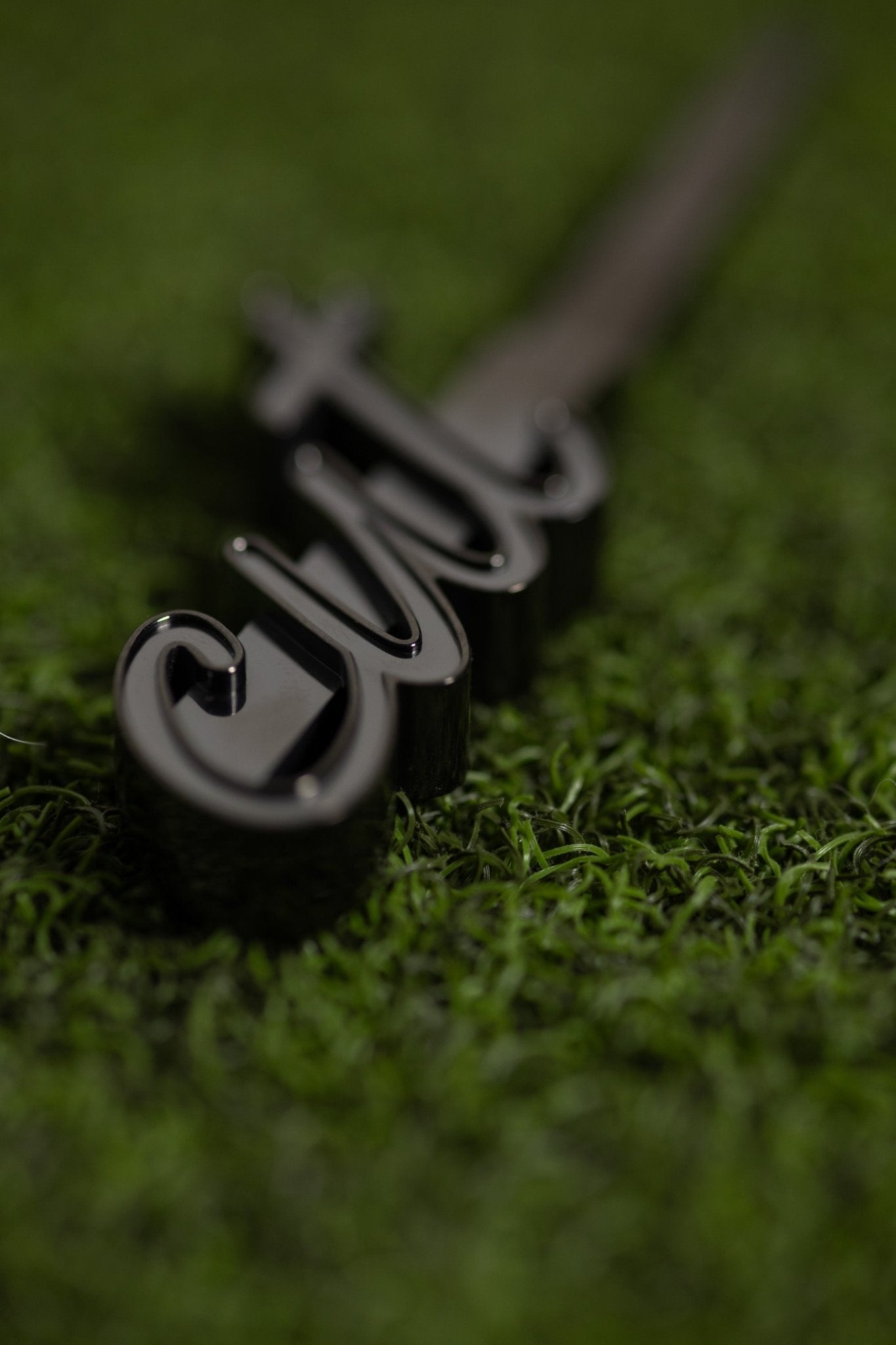 Black elegant CUT Script Black Divot Tool resting on green golf turf with stylish script detailing visible
