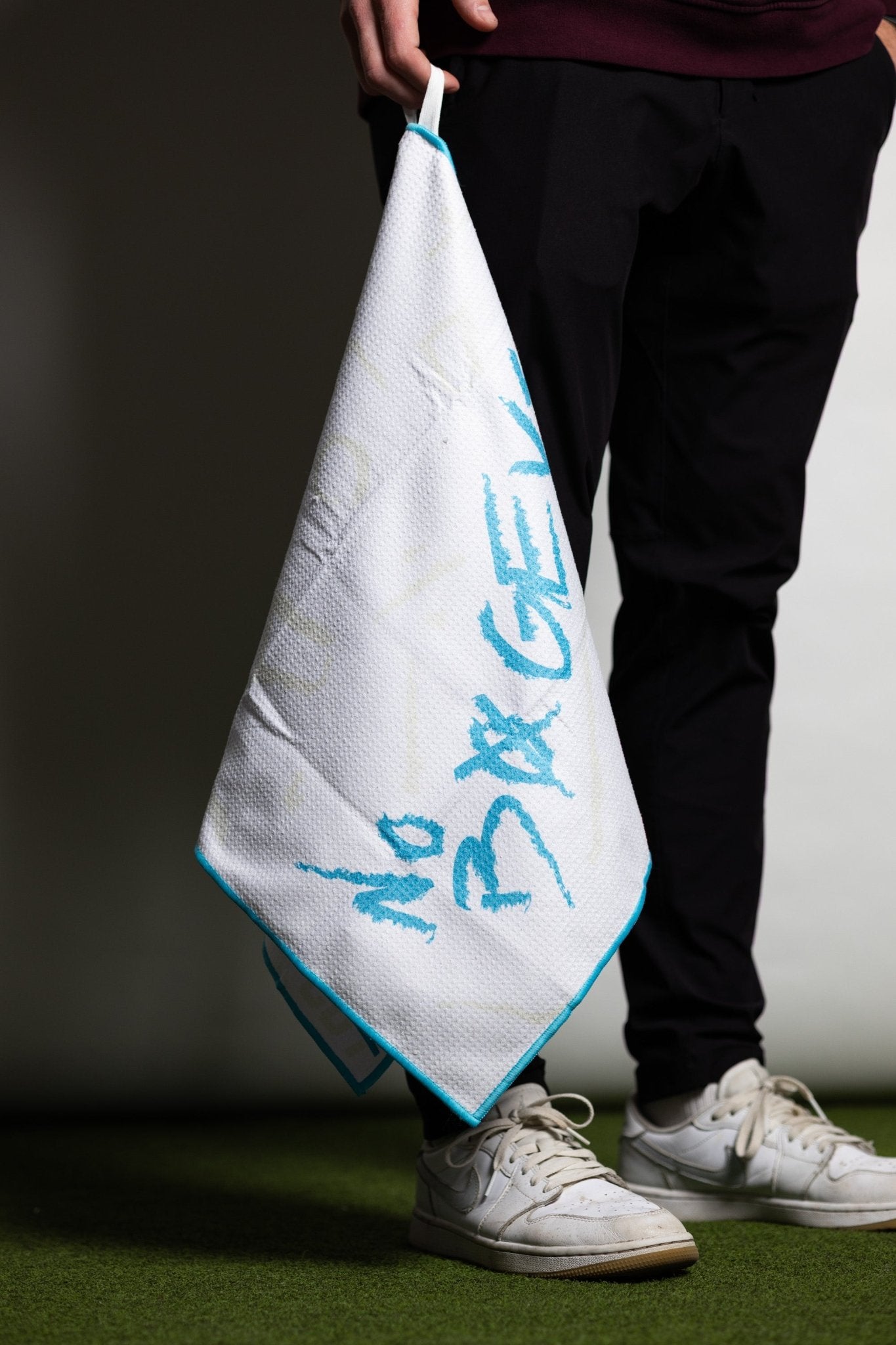 Person holding a white and blue No Bogeys Oversized Towel with casual black pants and white sneakers.