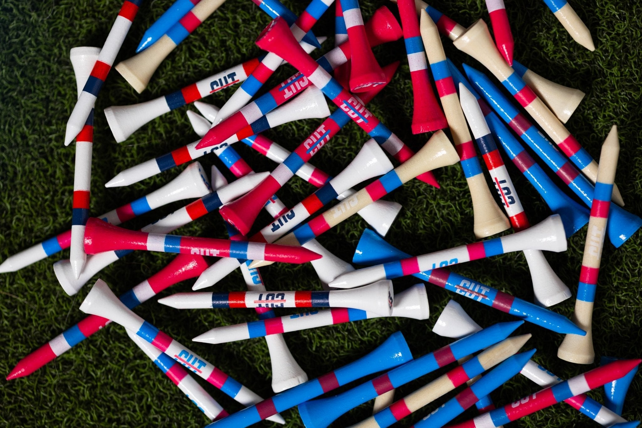 Multi Color 50 Pack Golf Tees scattered on green grass with red, blue, beige, and white accents and Cutline Golf Goods branding