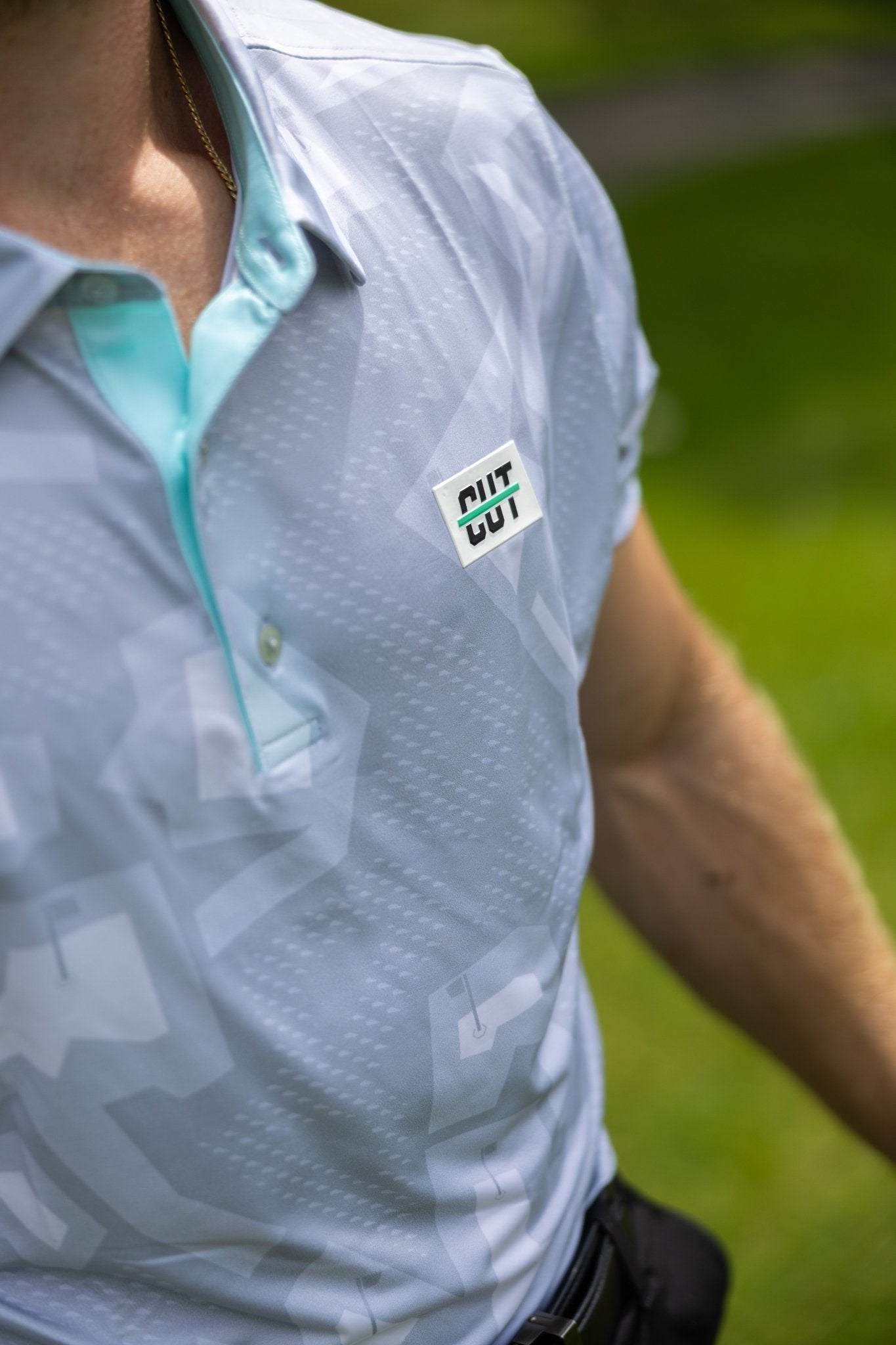 Close-up of a man wearing a light patterned Future Grey Pin Polo golf apparel shirt outdoors