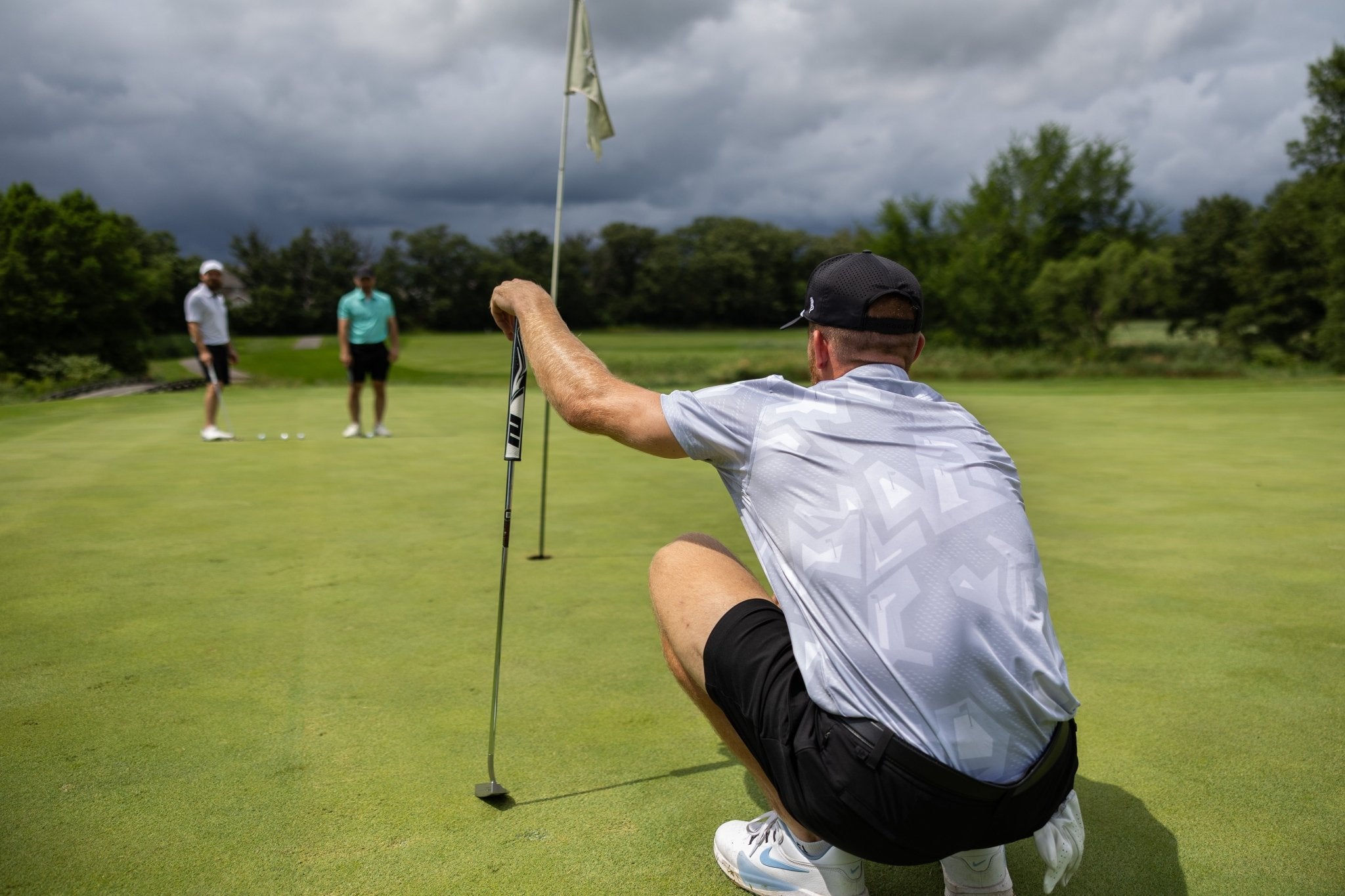 Man wearing Future Grey Pin Polo lining up a putt on a golf green with two players in the background