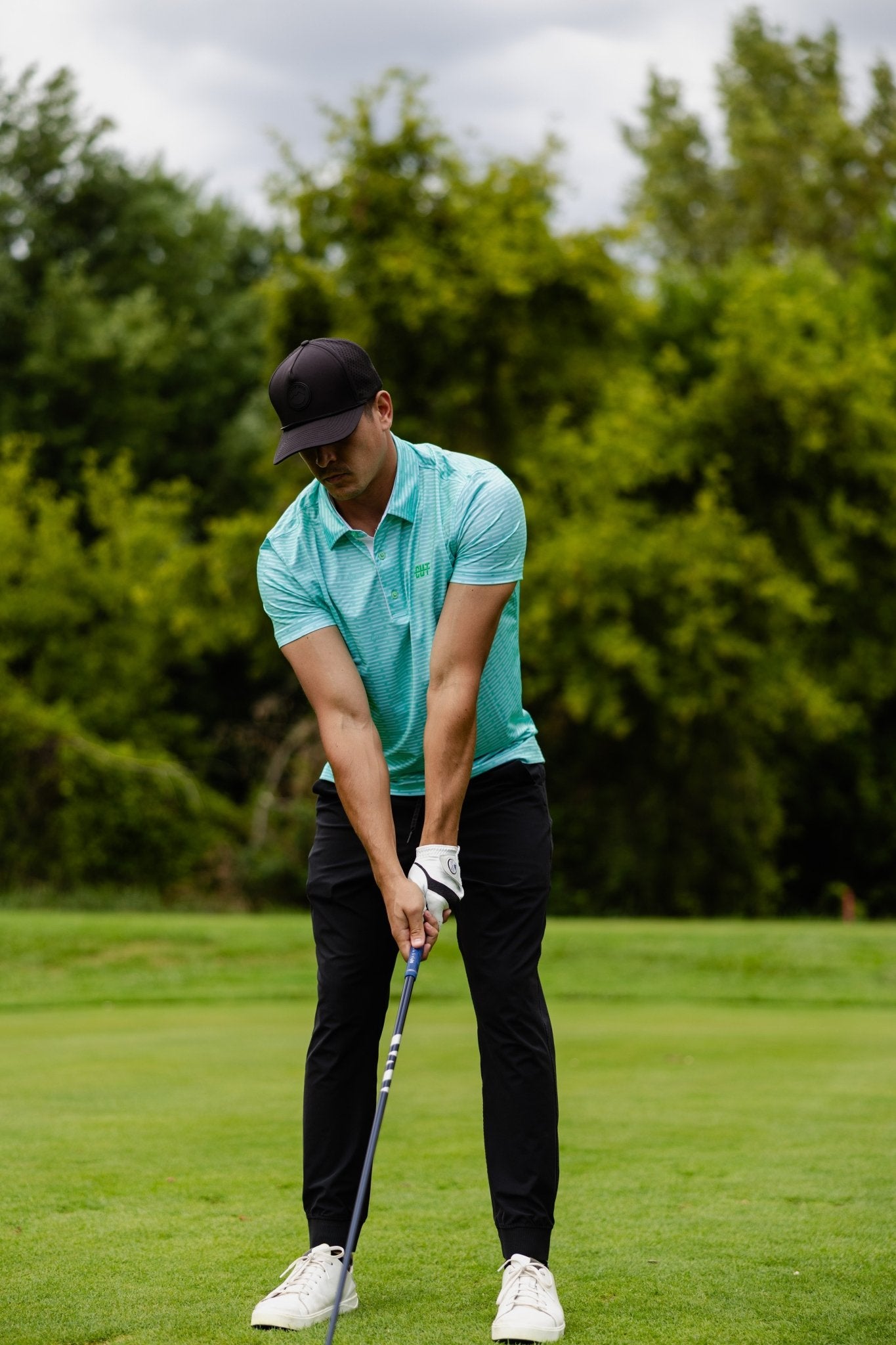 Man wearing a Minted Lines Polo preparing to swing golf club on a lush green golf course background