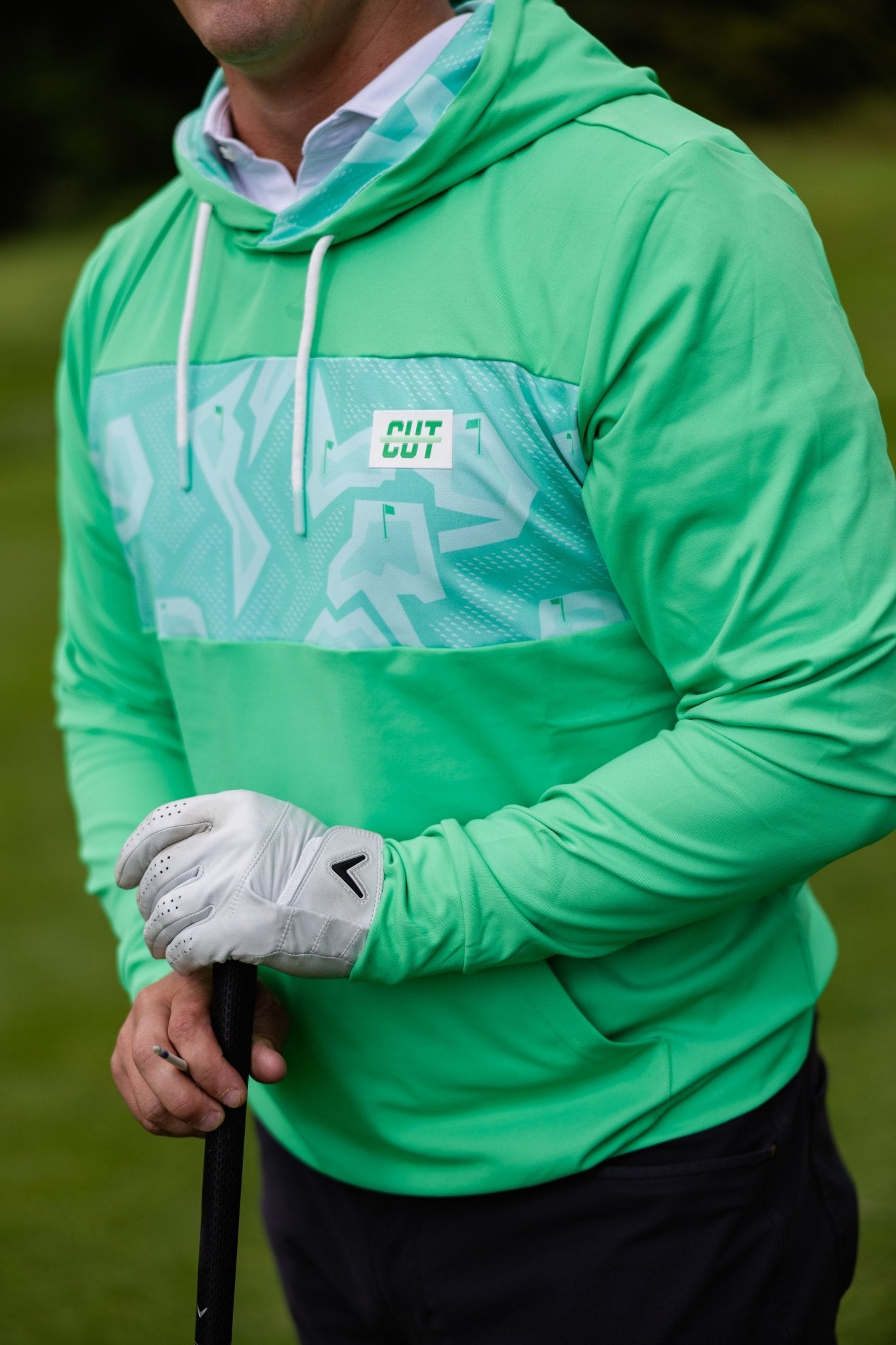 Man wearing Mint Future Tech Athletic Hoodie and golf glove holding a golf club on a green course