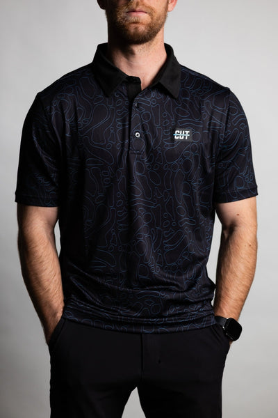 Man wearing a Midnight Teal Topo Polo with dark teal contour pattern and black collar, hands in pockets.