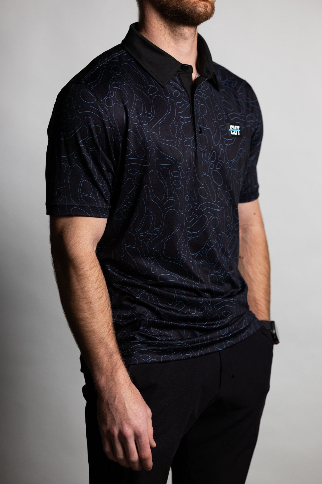 Man wearing a Midnight Teal Topo Polo with subtle topographic pattern and black collar, styled with black pants.