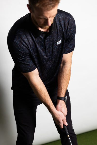 Man wearing Midnight Teal Topo Polo preparing to putt on indoor golf green in stylish golf apparel