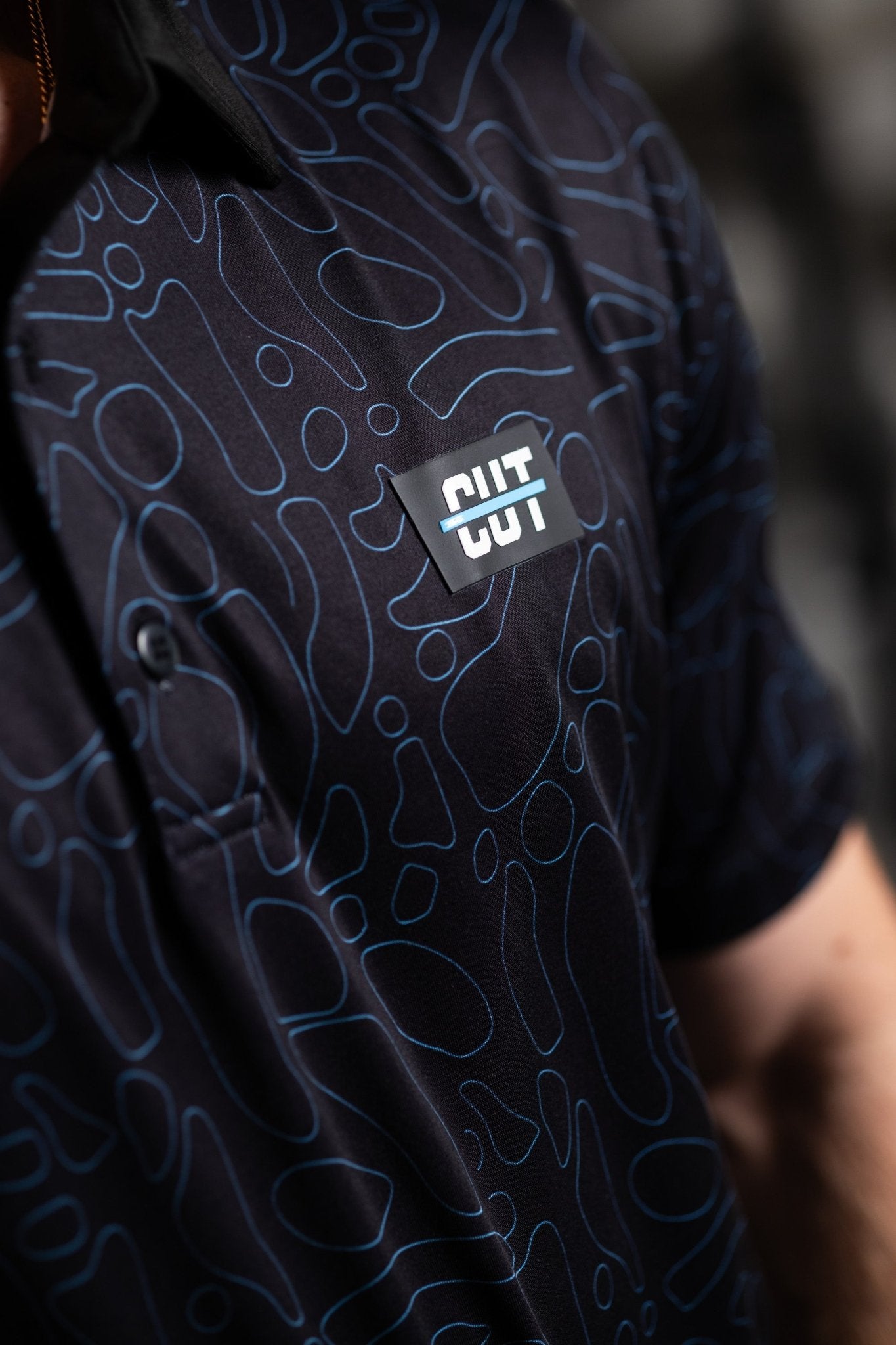 Close-up of a Midnight Teal Topo Polo with abstract teal pattern and Cutline Golf Goods logo patch on chest pocket.