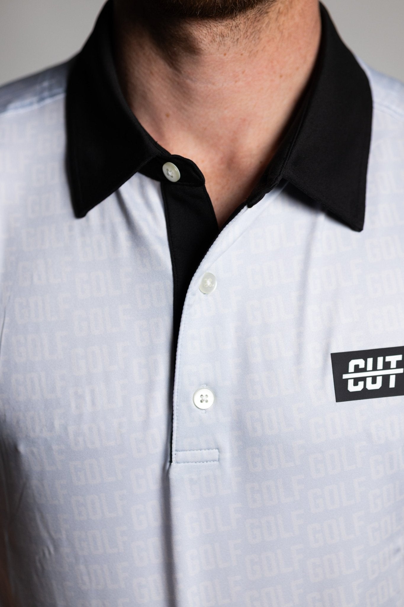 Close-up of a GOLF Pattern Off White Polo with a black collar and buttons, featuring subtle golf pattern and logo patch