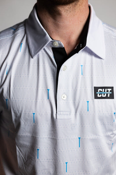 Close-up of a white golf polo with blue tees pattern and black collar label on a Teal "Tee" Polo