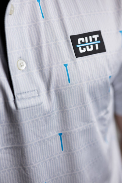 Close-up of a white golf polo with subtle blue tee patterns and Cutline Golf Goods logo, Teal "Tee" Polo style.