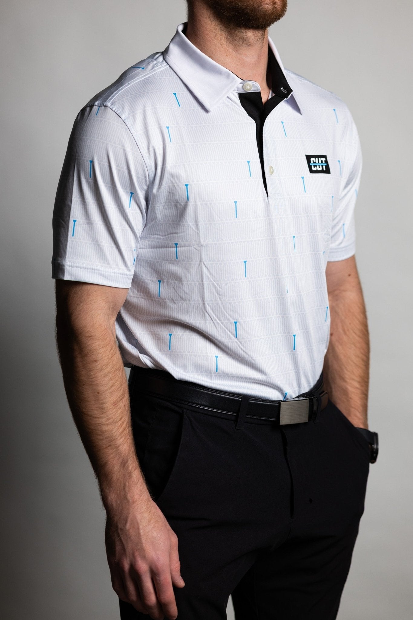 Man wearing a white patterned Teal "Tee" Polo with black pants in a studio setting