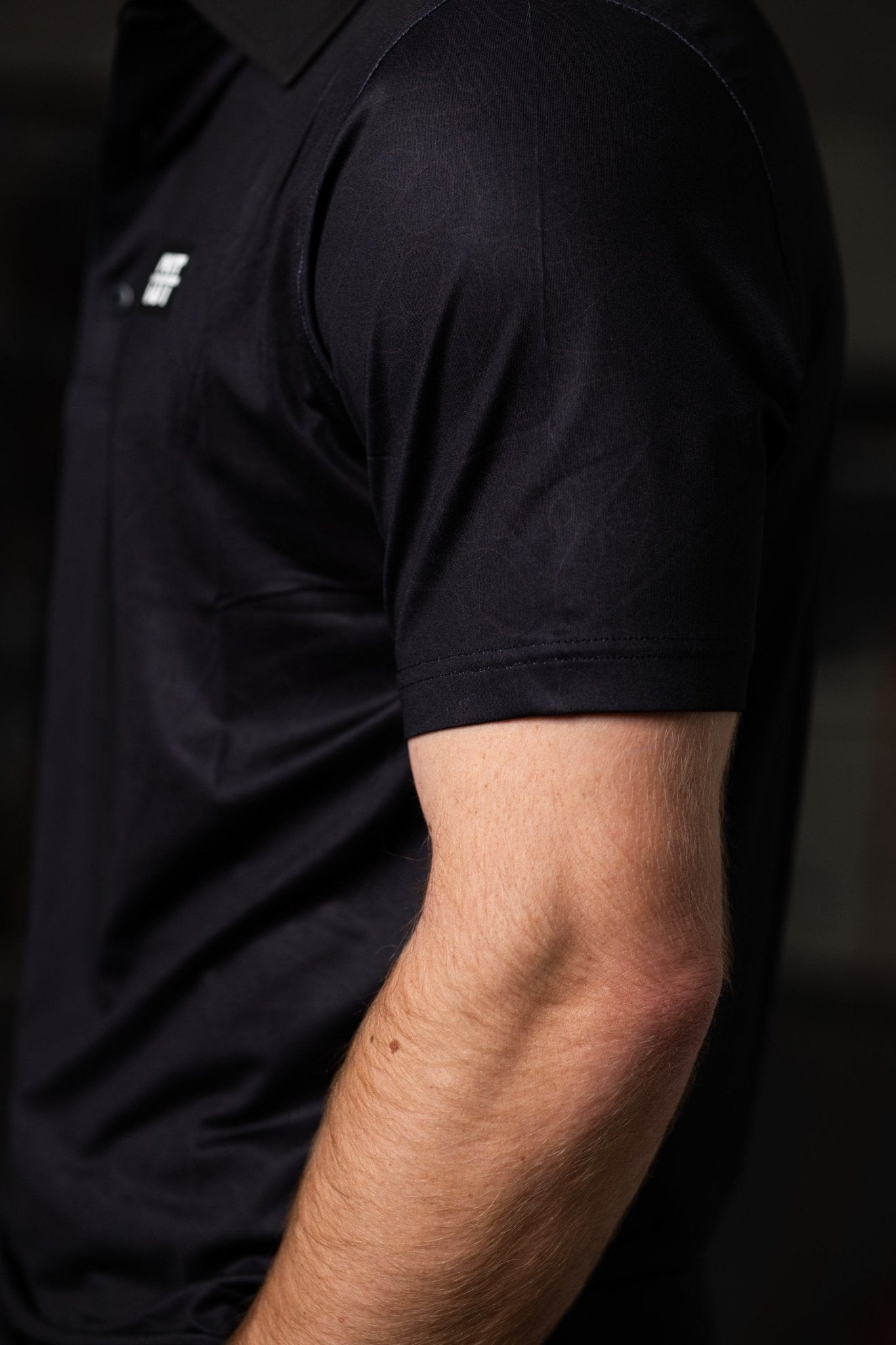 Close-up of a man wearing a Deep Topo Black Polo, showcasing the short sleeve and smooth fabric texture.