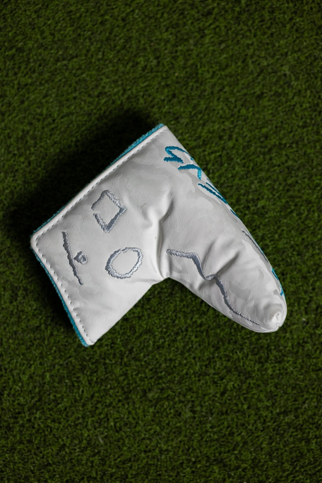 No Bogeys White Blade Cover with embroidered golf symbols resting on green turf background