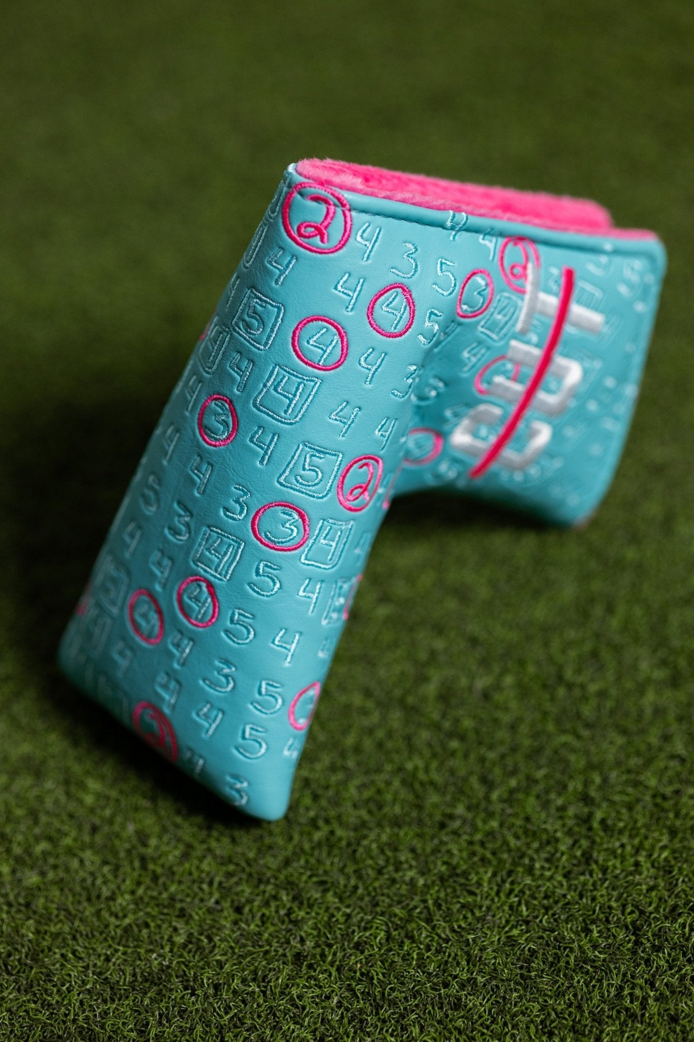 Scorecard Teal Blade golf putter cover with teal exterior and pink interior on green turf surface