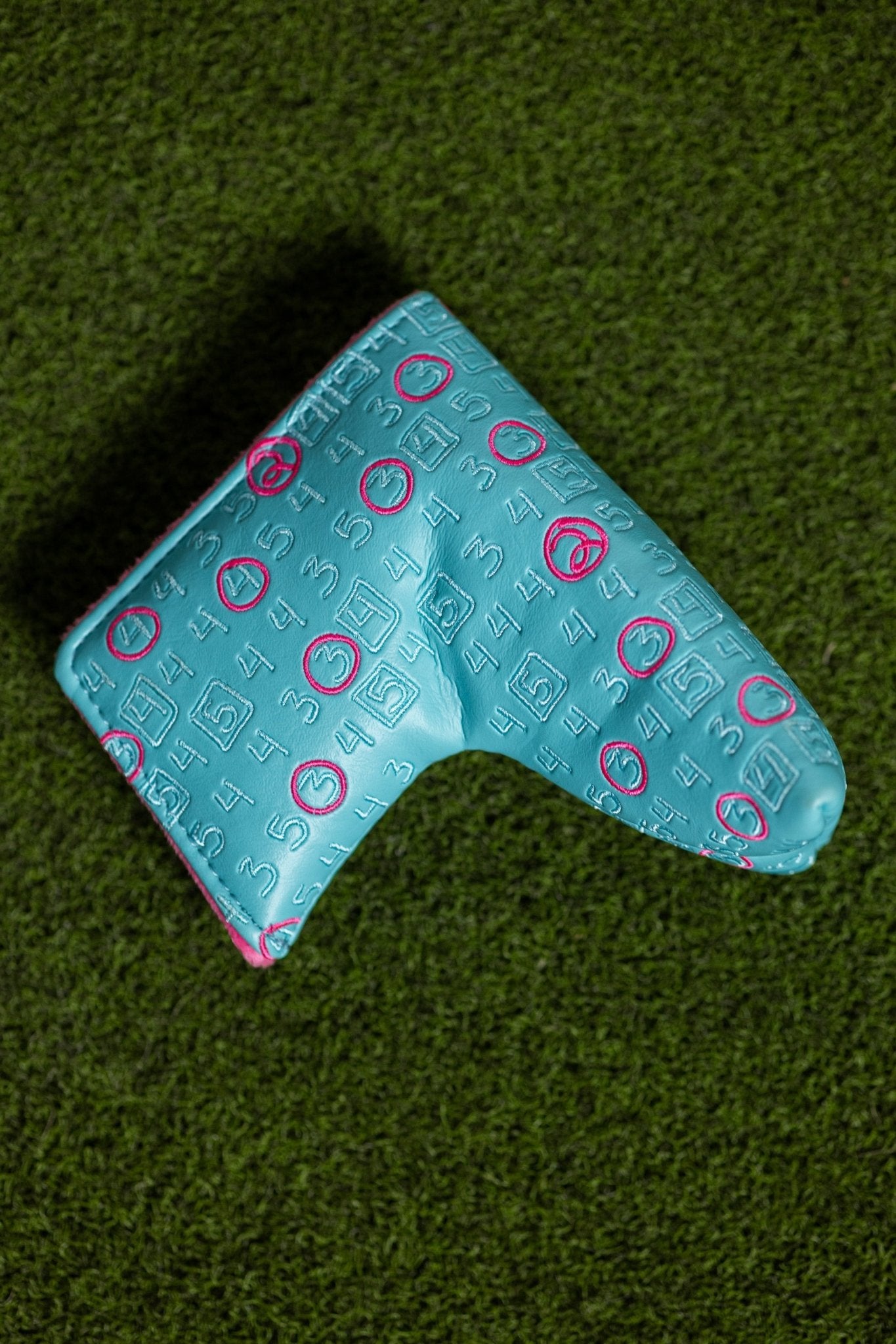 Scorecard Teal Blade golf putter cover with teal and pink stitching detail on green turf surface
