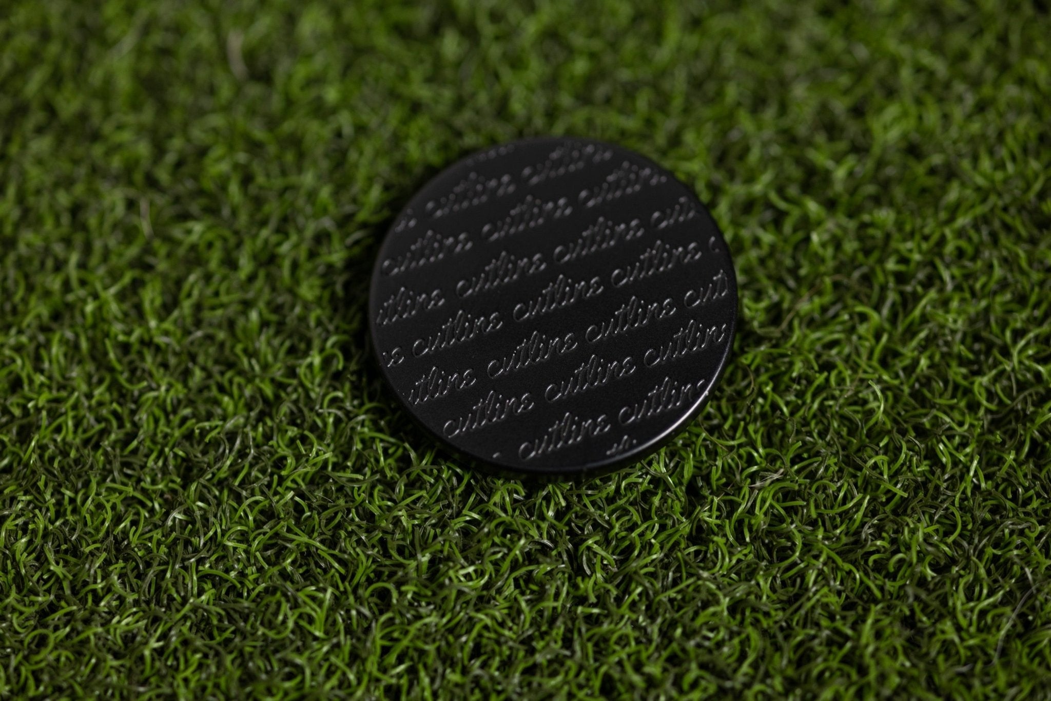 Cut "LINE" Alignment Ball Marker with repeated subtle branding pattern on golf green grass background
