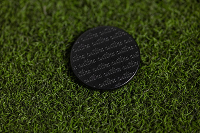 Cut "LINE" Alignment Ball Marker with repeated subtle branding pattern on golf green grass background
