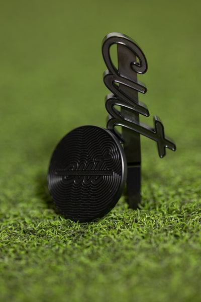 Cut "LINE" Alignment Ball Marker in black metal design resting on golf turf for precise putting alignment.