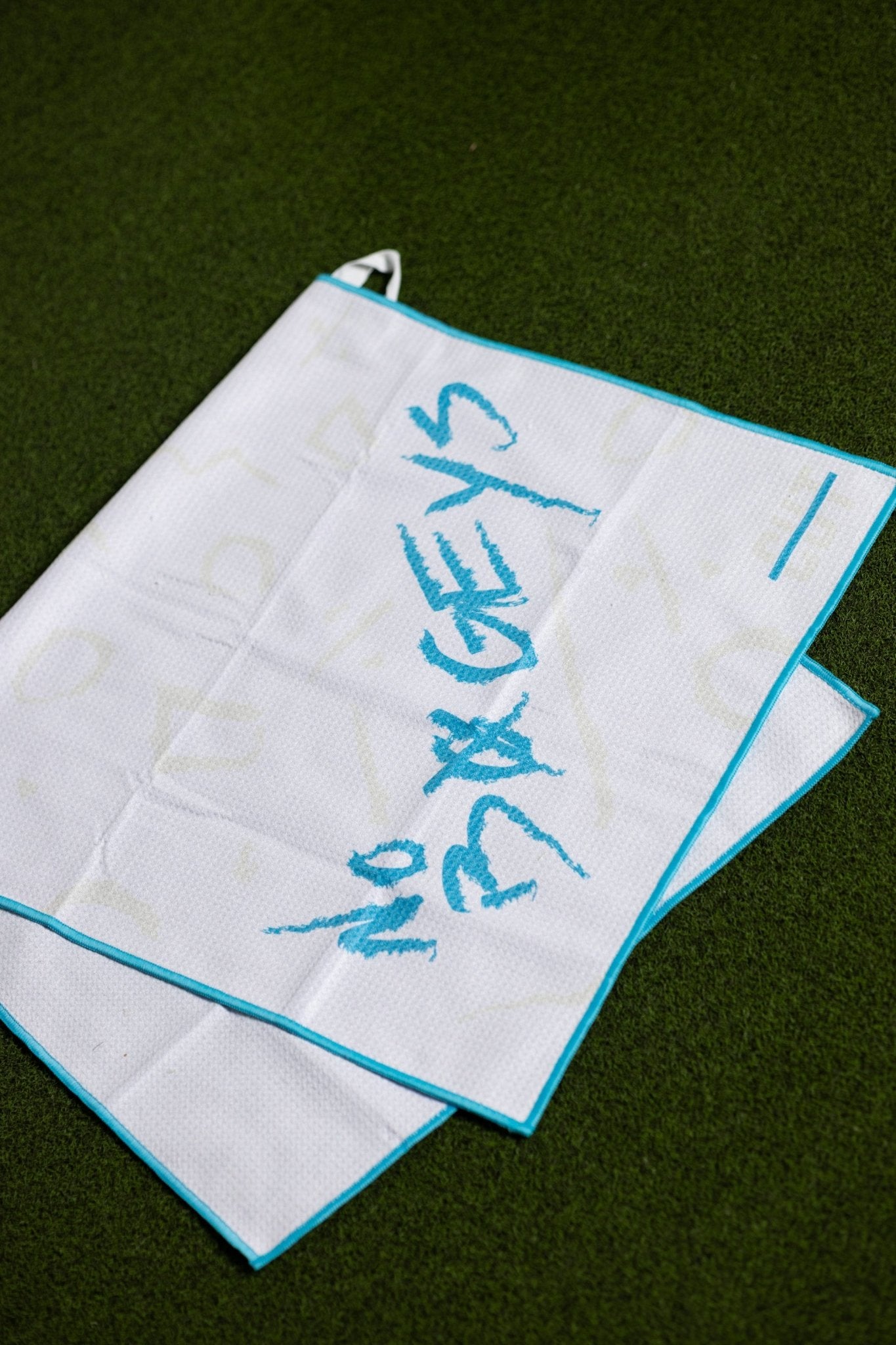 White golf towel with teal trim and "No Bogeys Oversized Towel" script laid on grass background