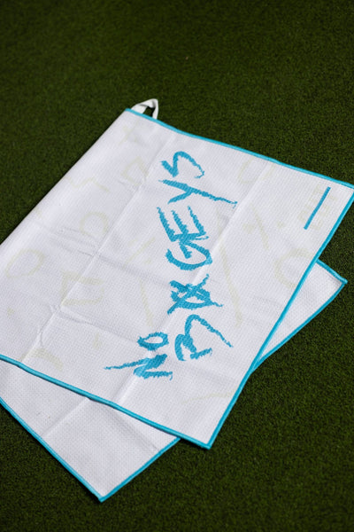 White golf towel with teal trim and "No Bogeys Oversized Towel" script laid on grass background
