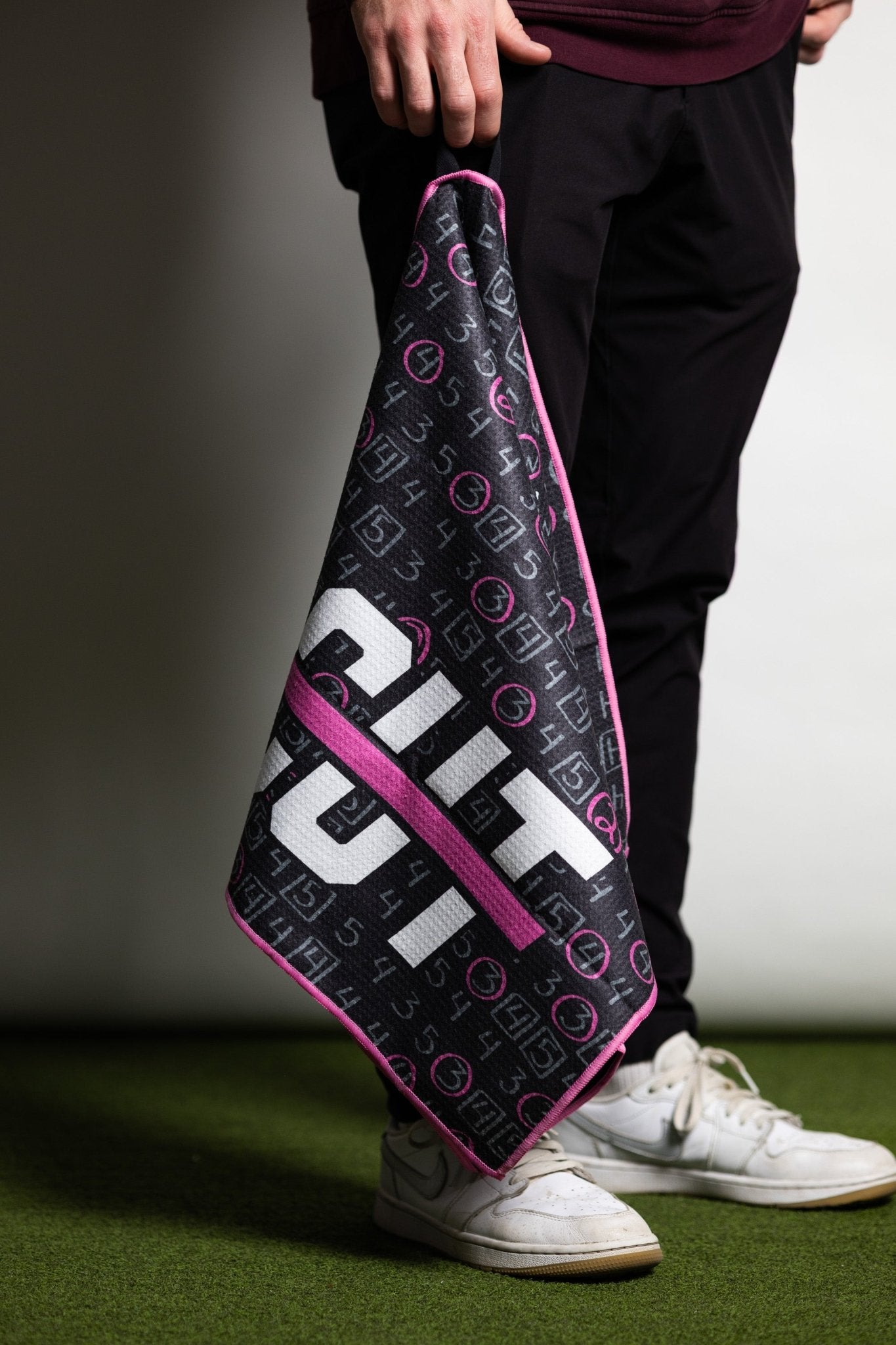 Person holding a black and pink Pink Scorecard Oversized Towel with golf scoring design on green turf.