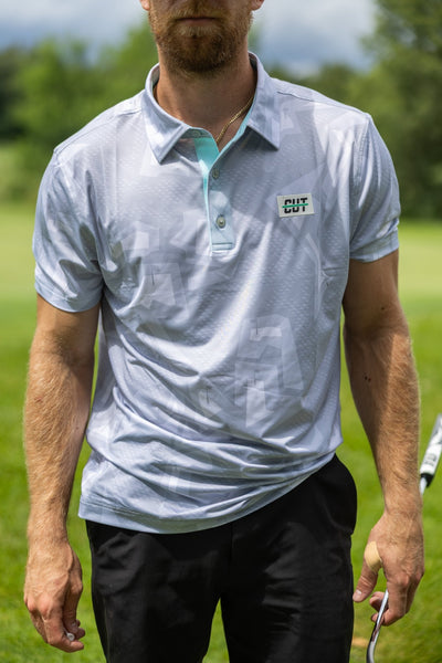 Man wearing Future Grey Pin Polo golf shirt outdoors holding a golf club on a sunny day