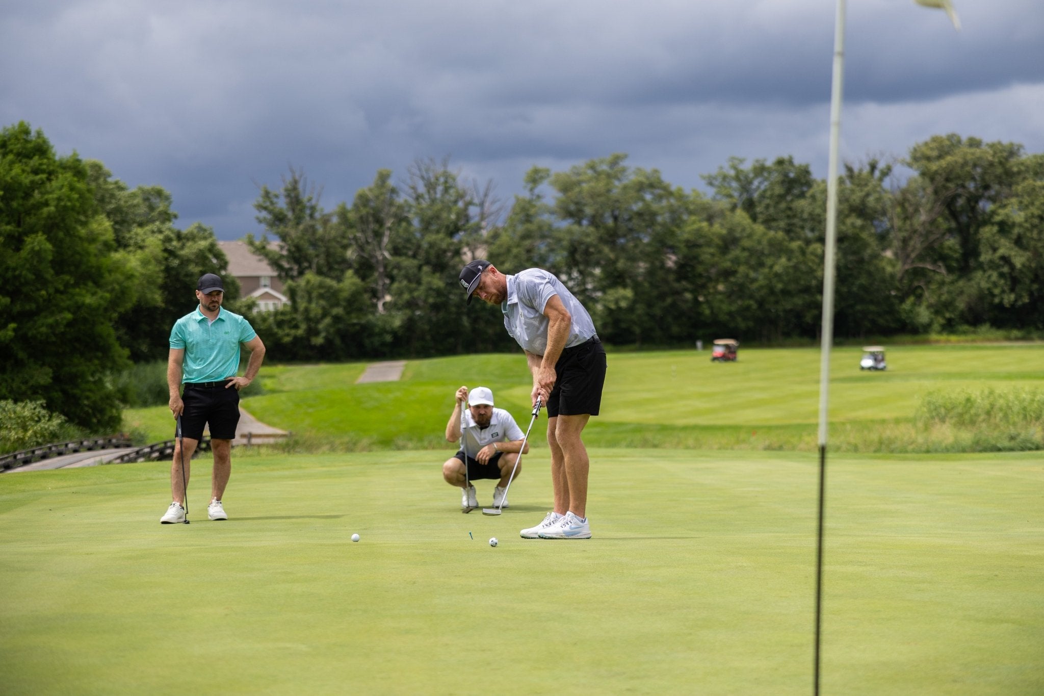 Three men playing golf on a green with one putting wearing a Future Grey Pin Polo golf apparel shirt