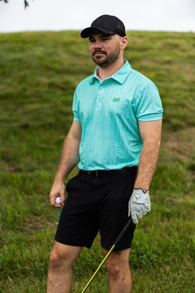 Man wearing Minted Lines Polo in mint green with black shorts and golf glove holding golf club on grassy course