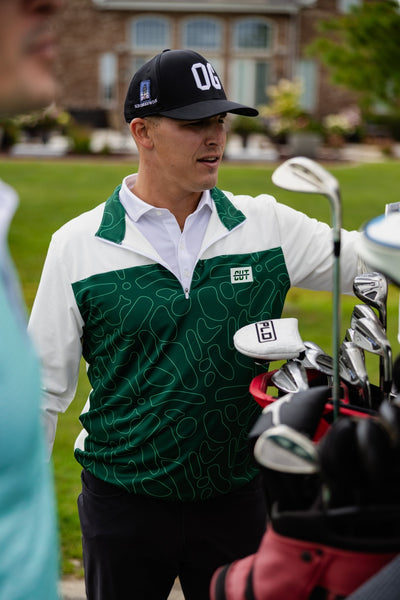 Man wearing Green Topo Athletic Q-Zip golf apparel standing next to a golf bag filled with clubs outdoors