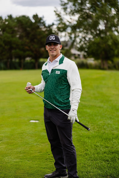 Man wearing Green Topo Athletic Q-Zip golf apparel standing on golf course holding golf club smiling