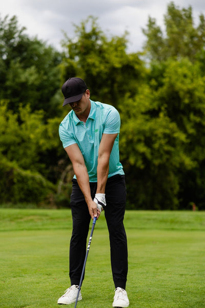 Man wearing a Minted Lines Polo preparing to swing golf club on a lush green golf course background
