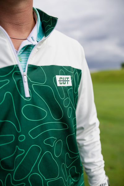 Close-up of a Green Topo Athletic Q-Zip golf pullover with abstract green pattern on a golf course background