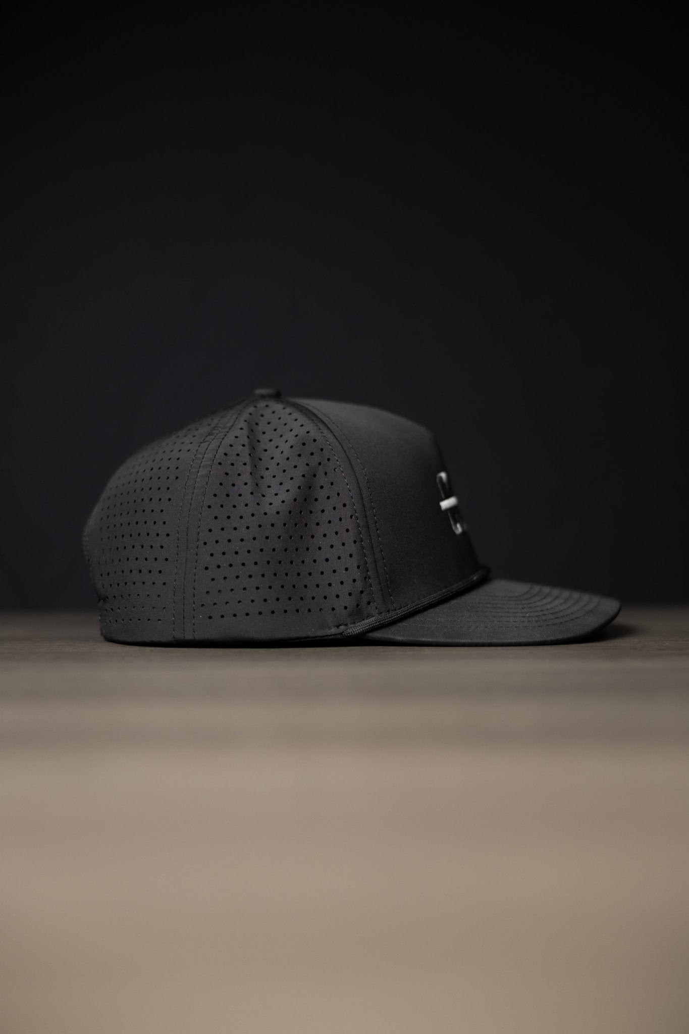 Blackout Cutline Hat in black with perforated panels and curved brim against dark background.