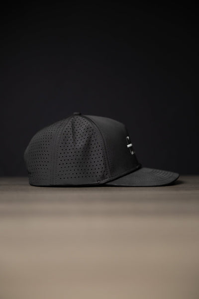 Blackout Cutline Hat in black with perforated panels and curved brim against dark background.