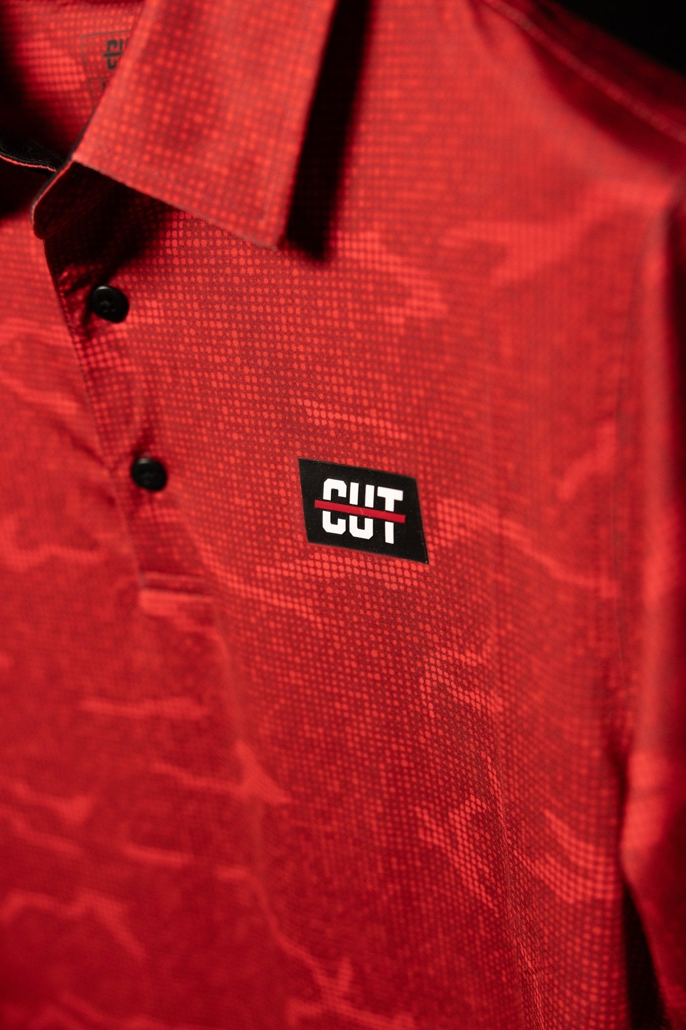 Close-up of a True Red Tech Camo Polo with subtle camo pattern and black buttons on golf apparel polo shirt